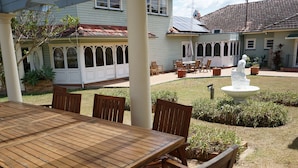 A covered patio with a wooden table and chairs, a white fountain, and a garden area with potted plants. - Melville House (Lismore)