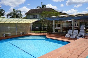 A swimming pool with a tiled deck, a covered seating area, and a fenced garden. - Melville House (Lismore)