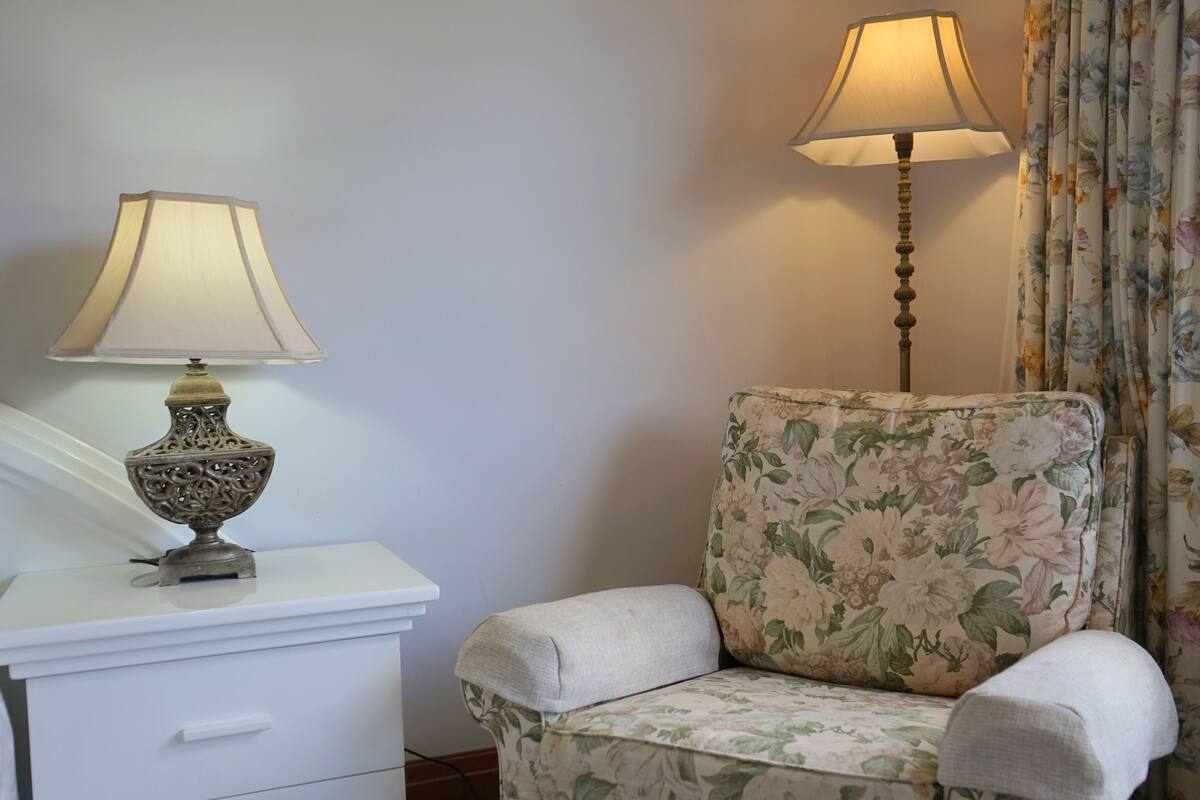 Une pièce avec une table de chevet blanche, un fauteuil à motifs floraux et un lampadaire.