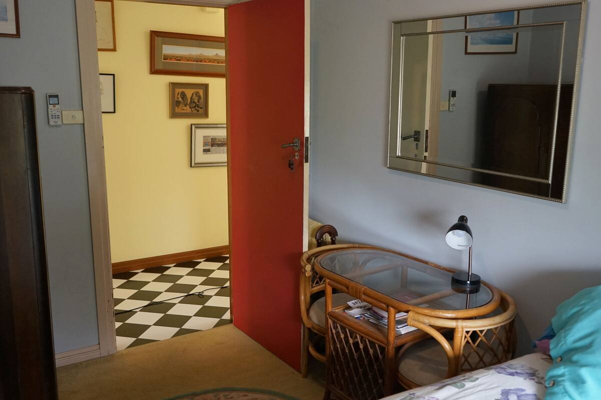 Une pièce avec un sol à carreaux, une table avec un plateau en verre et une lampe, un lit avec une literie à motifs floraux et un miroir au mur.