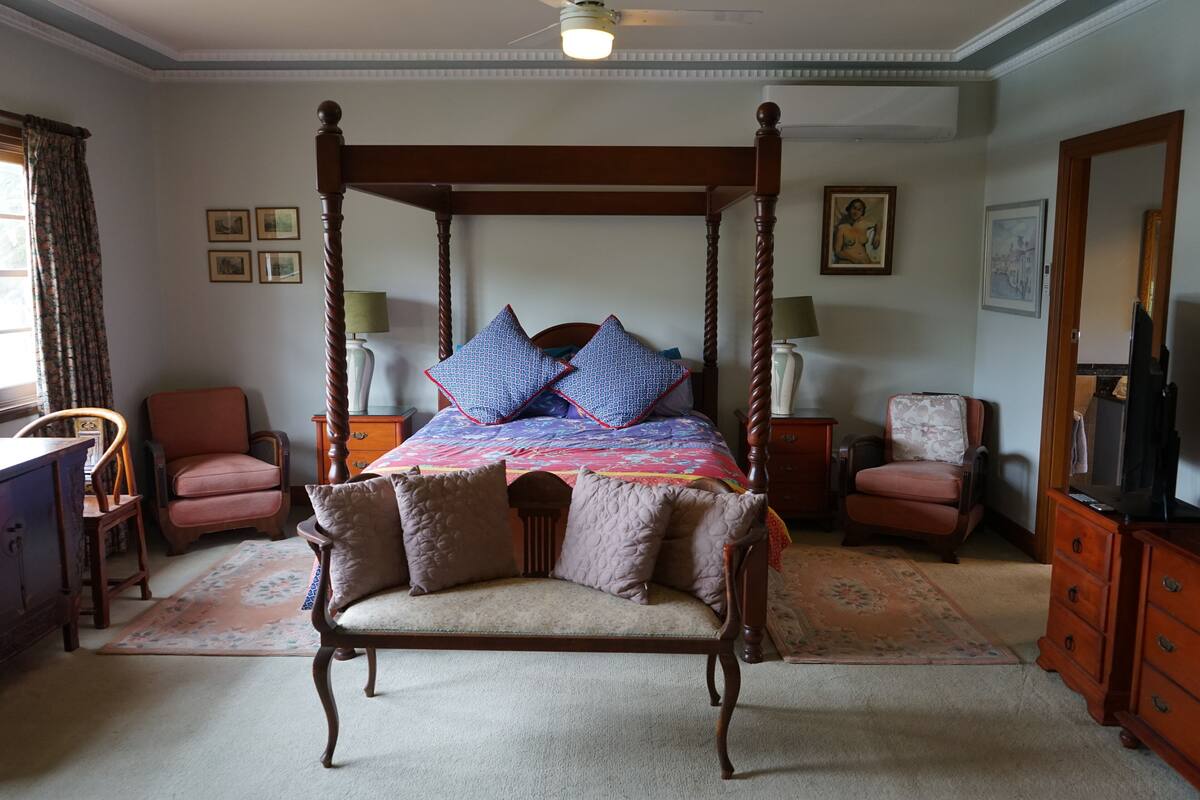 Un lit à baldaquin avec une courtepointe aux couleurs vives, deux fauteuils, un banc en bois et une commode.