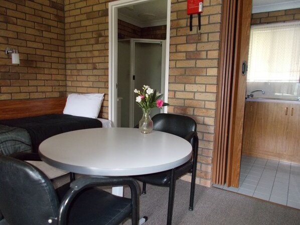 Una habitación compacta con una mesa redonda, dos sillas, un sofá y una pequeña zona de cocina con un lavamanos y armarios.