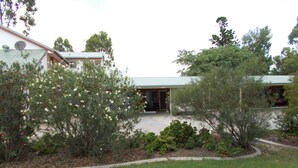 A house with a covered porch, surrounded by various shrubs and trees. - Park House Motor Inn (Oakey)