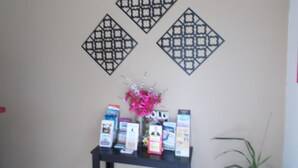 A wall with three decorative metal panels and a small table with magazines and a vase of flowers. - Park House Motor Inn (Oakey)