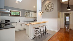 A modern kitchen with white cabinetry, a wooden island with bar stools, a large wall clock, and a skylight. - Oak Tree Lodge (Rhyll)