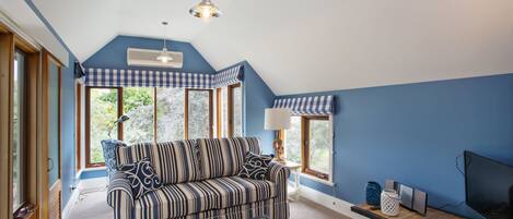 A room with a blue and white striped sofa, a wooden table with a lamp, and a television.