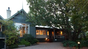 A wooden house with a gravel driveway, large windows, and a tree in the foreground. - Oak Tree Lodge (Rhyll)