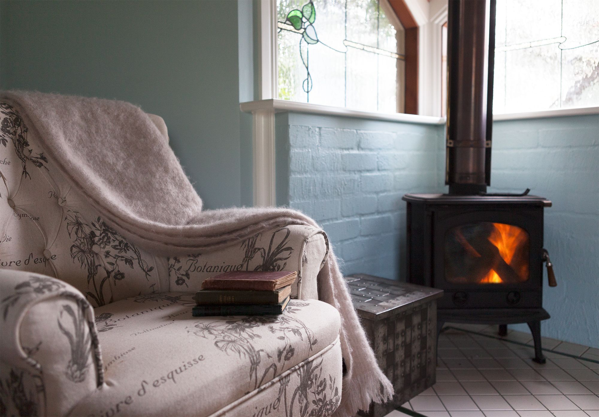 A cozy room with a vintage sofa, a fireplace, and a window with floral stained glass.