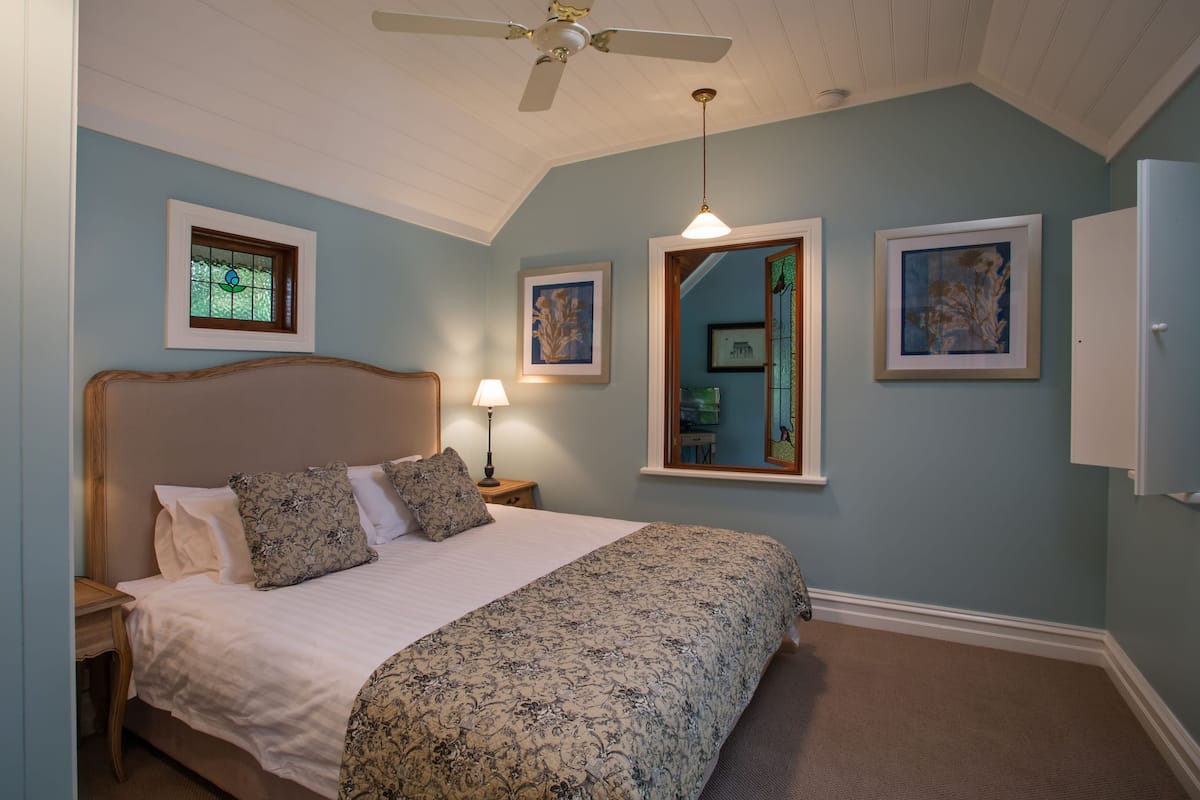 A bedroom with a bed, a ceiling fan, a nightstand, a lamp, and framed artwork on the walls.