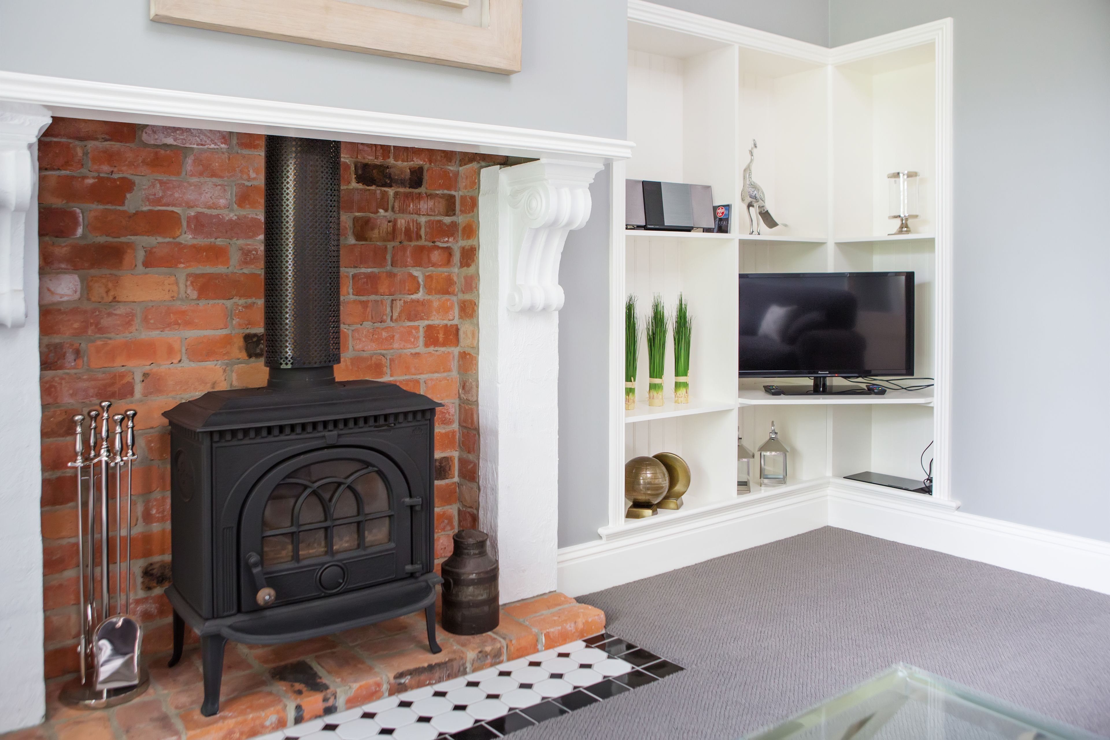 A living room with a brick fireplace, a television on a white shelf, and a patterned rug.