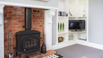 A living room with a brick fireplace, a television on a white shelf, and a patterned rug.