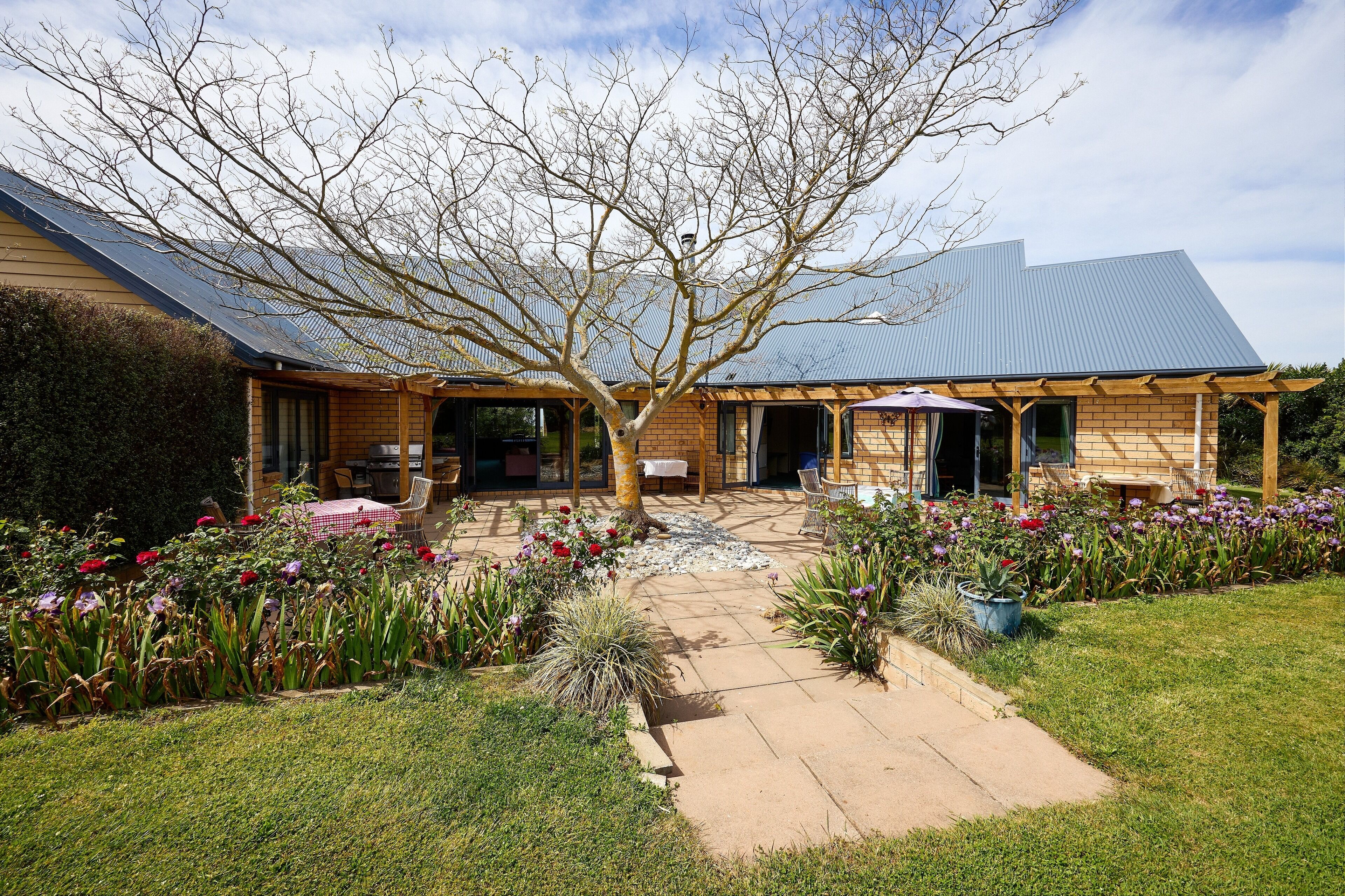 A house with a covered patio, a garden with flowers, and a brick exterior.