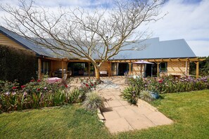 A house with a covered patio, a garden with flowers, and a brick exterior.