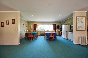 A compact kitchen with a refrigerator, stove, and cabinets. There is a dining area with a table and chairs, and a window with curtains.
