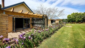 A house with a brick exterior, a wooden pergola, and a well-maintained garden with purple flowers. - Awatea Country B&B (Hapuku)