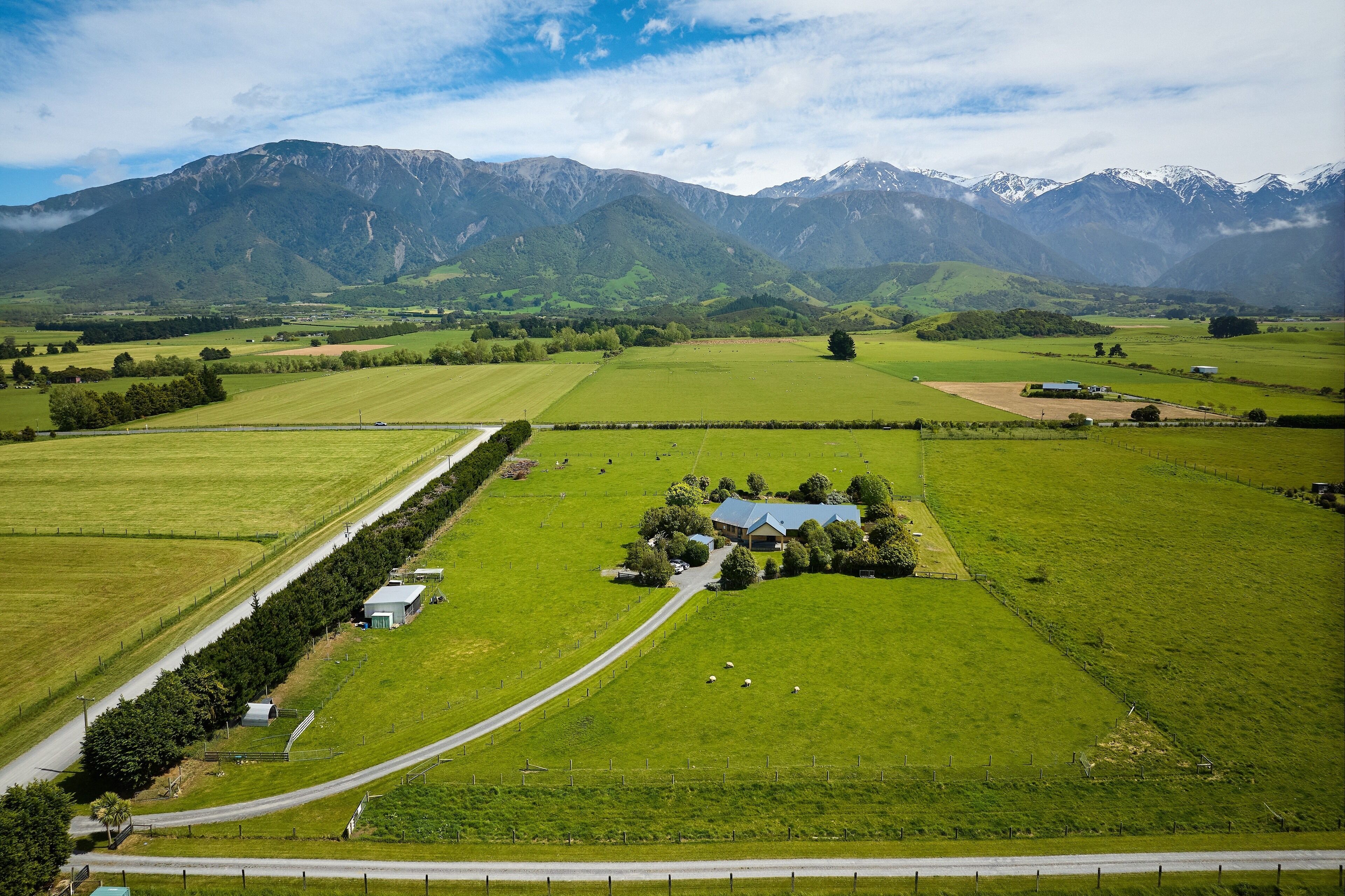 A rural landscape with a farmhouse surrounded by fields and mountains.