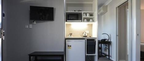 Una kitchenette compacta con microondas, refrigerador y una pequeña mesa.