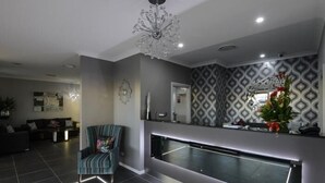 A modern living room with a large sofa, a striped armchair, and a built-in entertainment unit with a TV. - Aastro Dish Motor Inn (Parkes)
