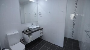 A modern bathroom with a white toilet, a sink with a mirror above it, and a shower area with a vertical strip of text on the wall. - Aastro Dish Motor Inn (Parkes)