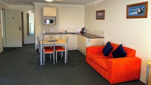 En kompakt opholdsstue med tekøkken, spiseplads og en lys orange sofa.
