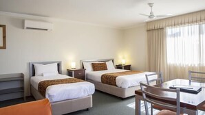 Et hotelværelse med to senge, et spisebord og en ventilator.