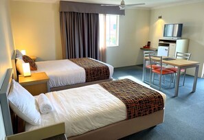 Una habitación de hotel con dos camas, un escritorio con silla, televisión y ventana con cortinas.