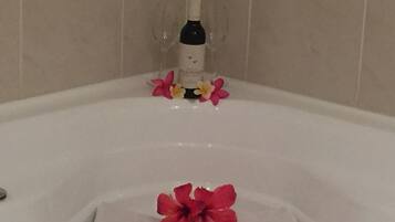 A bathtub with a bottle of shampoo and a few flowers.