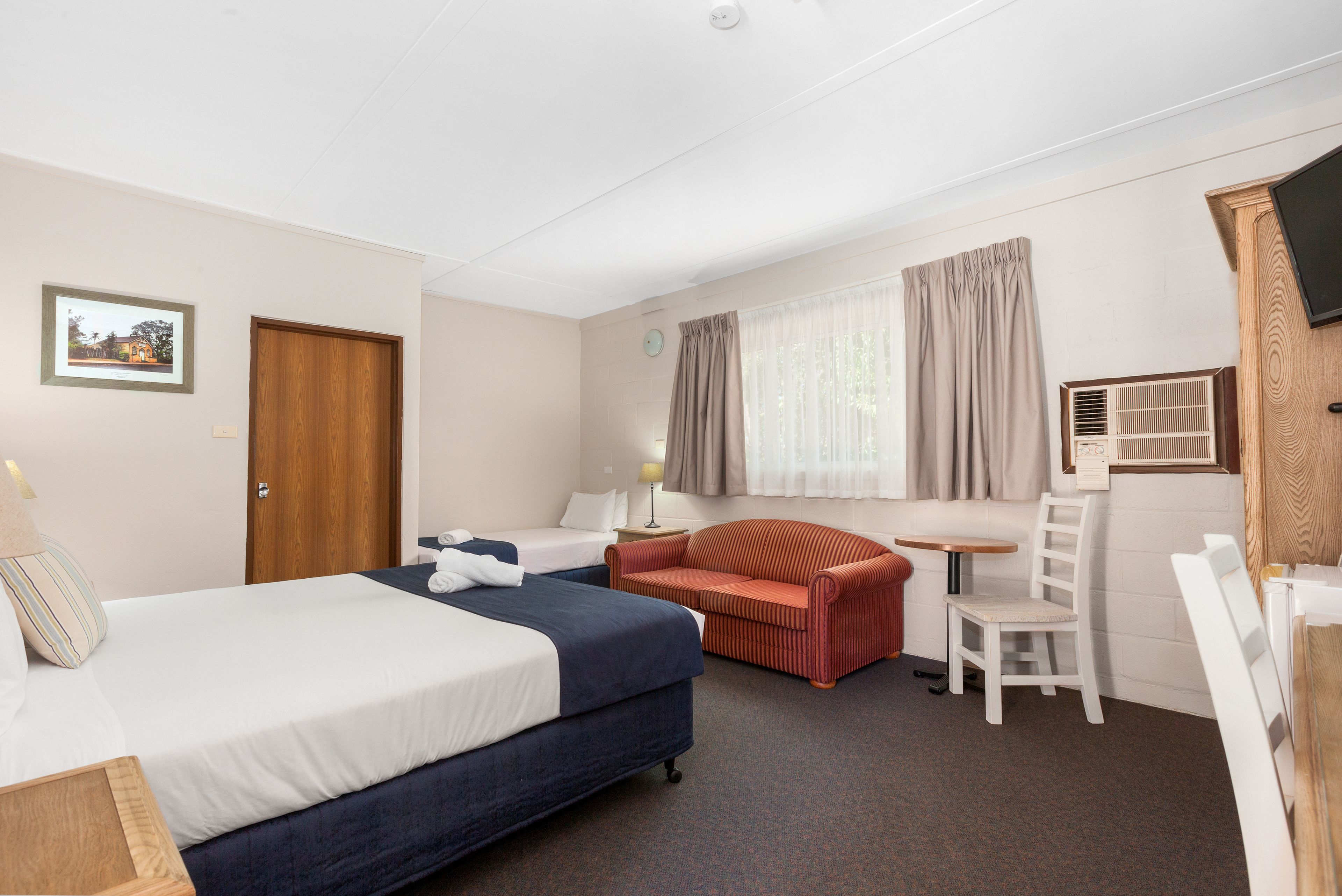 A hotel room with a bed, a sofa, a chair, a small table, and a TV.