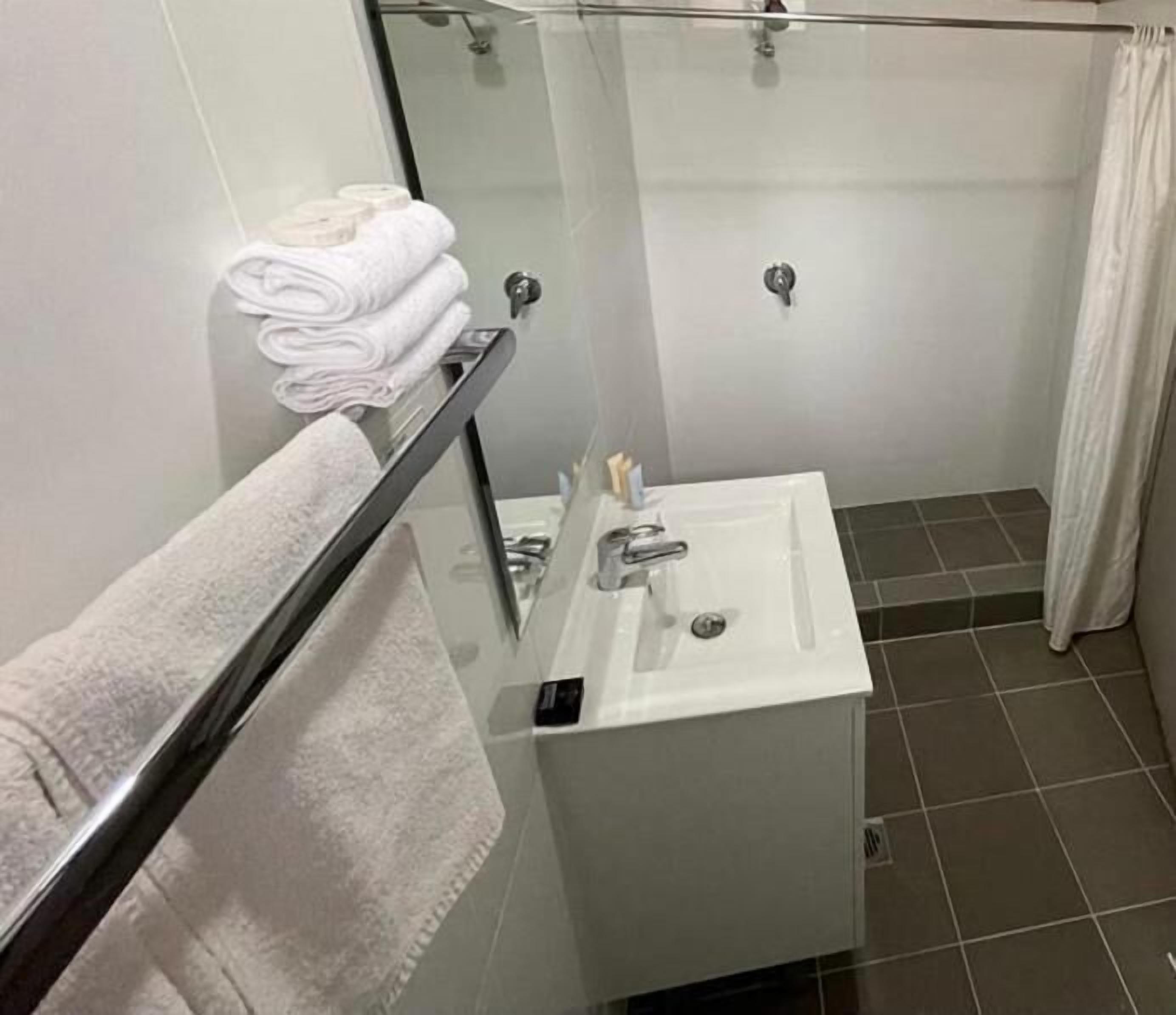 A bathroom with a glass shower enclosure, a white sink with a mirror, and a towel rack with folded towels.