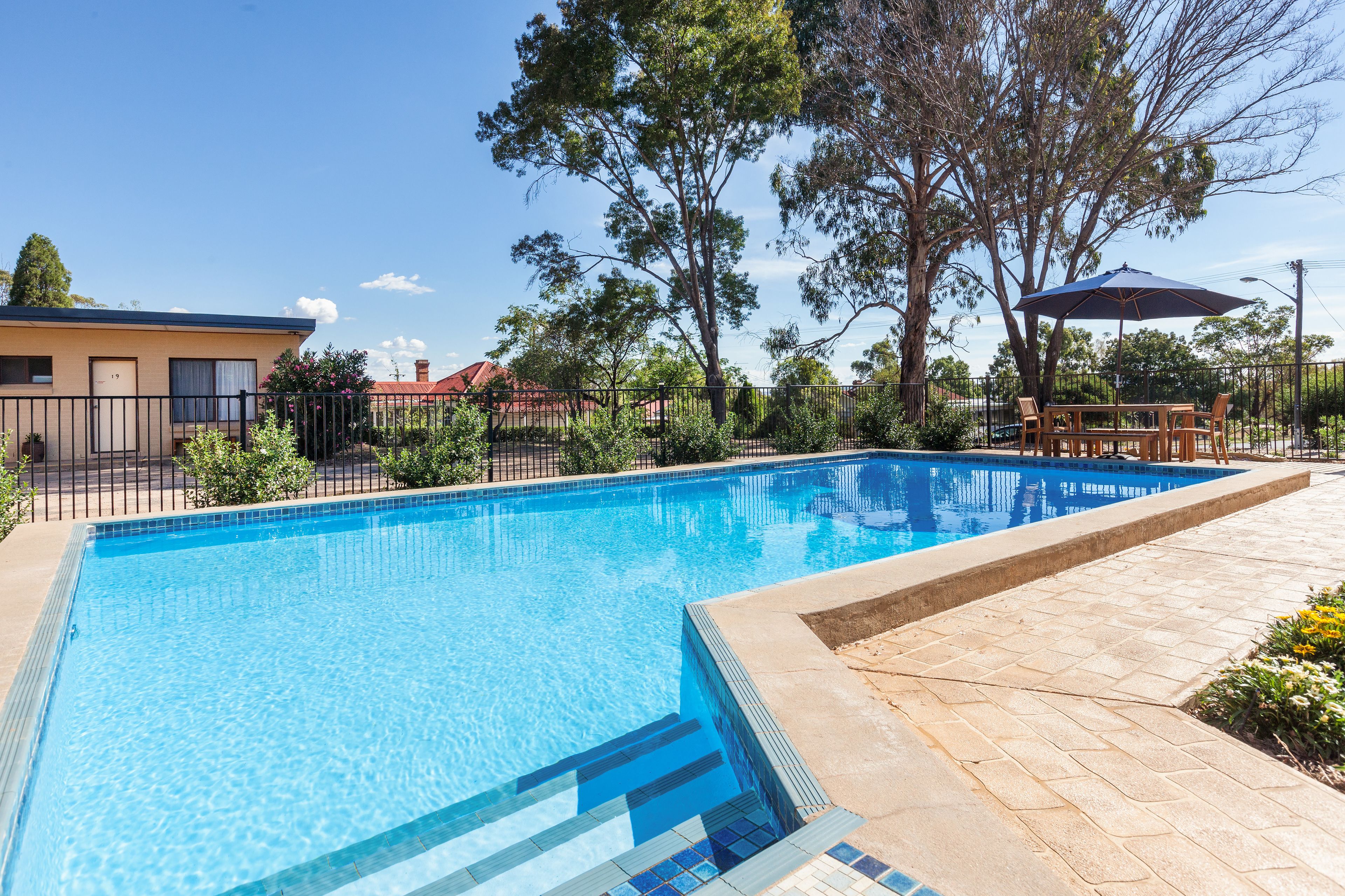 Una piscina rectangular con agua azul cristalina, rodeada por un solado de baldosas y una valla.