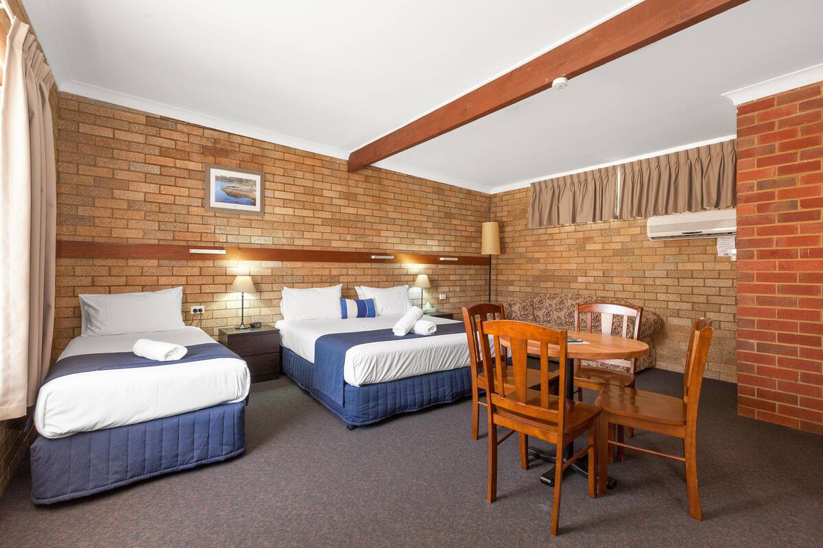 Quarto de hotel com duas camas, uma mesinha e uma cadeira.