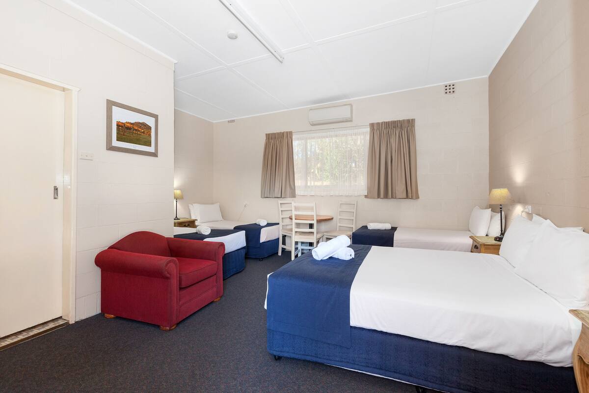 Quarto de hotel com uma cama grande, duas camas de solteiro, uma poltrona vermelha, uma mesa e uma cadeira.