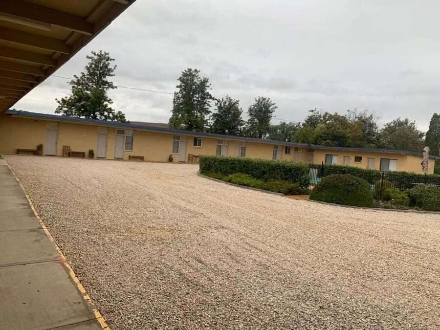 A motel with a gravel driveway, a covered parking area, and a row of rooms with windows.