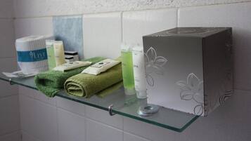 Un estante de baño con artículos de aseo, una toalla verde y una caja con diseño floral.