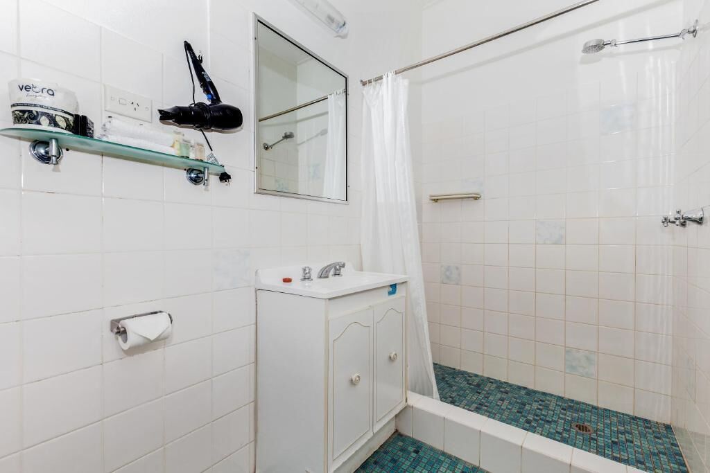 A bathroom with a shower, a sink, a mirror, and a hairdryer on a shelf.