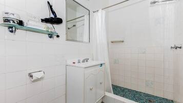 A bathroom with a shower, a sink, a mirror, and a hairdryer on a shelf.