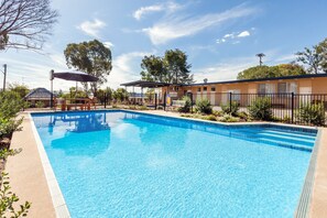 A rectangular swimming pool with a tiled edge, surrounded by a fence and greenery. - Gulgong Motel (Gulgong)