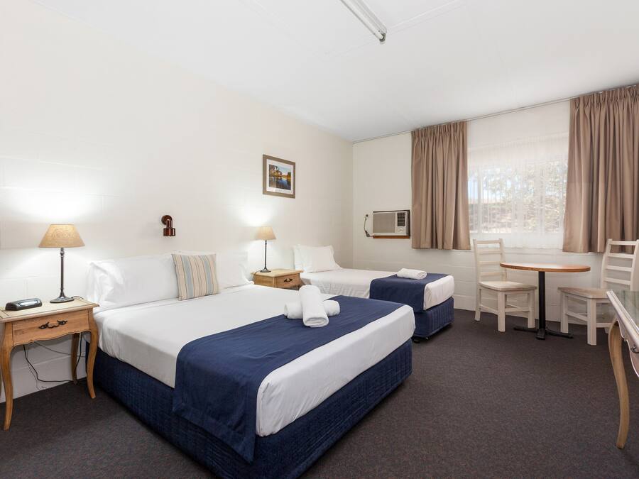 Camera d'albergo con due letti, una scrivania, una sedia, una lampada, un quadro appeso al muro e una finestra con tende.