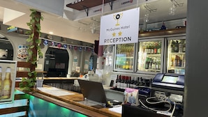 A reception area with a sign for McGuires Hotel, a counter with a laptop, and a display of bottled beverages. - McGuire's CBD Hotel (Mackay)