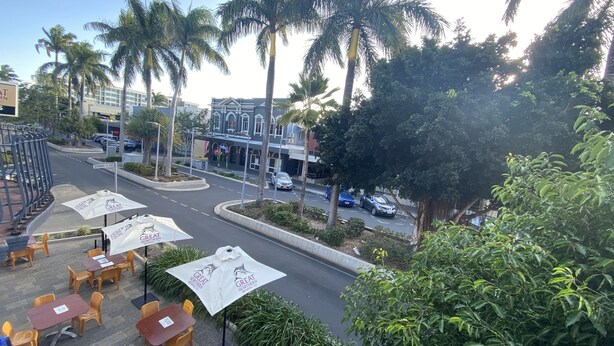 A street view with outdoor seating, palm trees, and a building with a sign. - McGuire's CBD Hotel (Mackay)