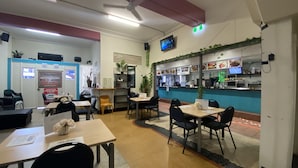 A restaurant with tables and chairs, a counter with food displays, and a TV screen. - McGuire's CBD Hotel (Mackay)