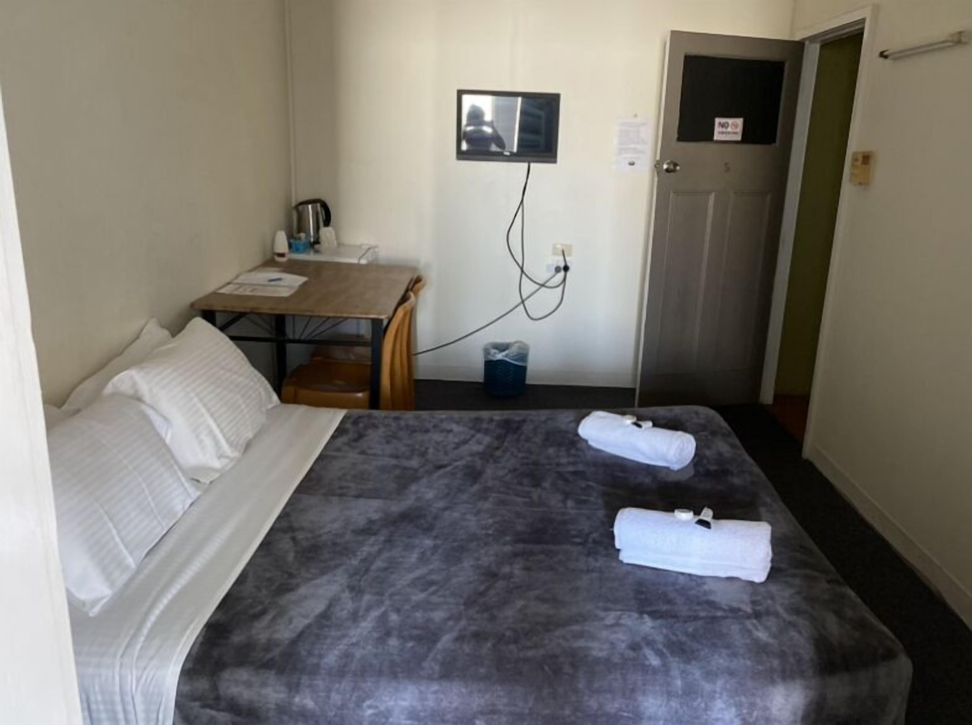 Una habitación de hotel con cama, escritorio, silla, televisor y puerta.