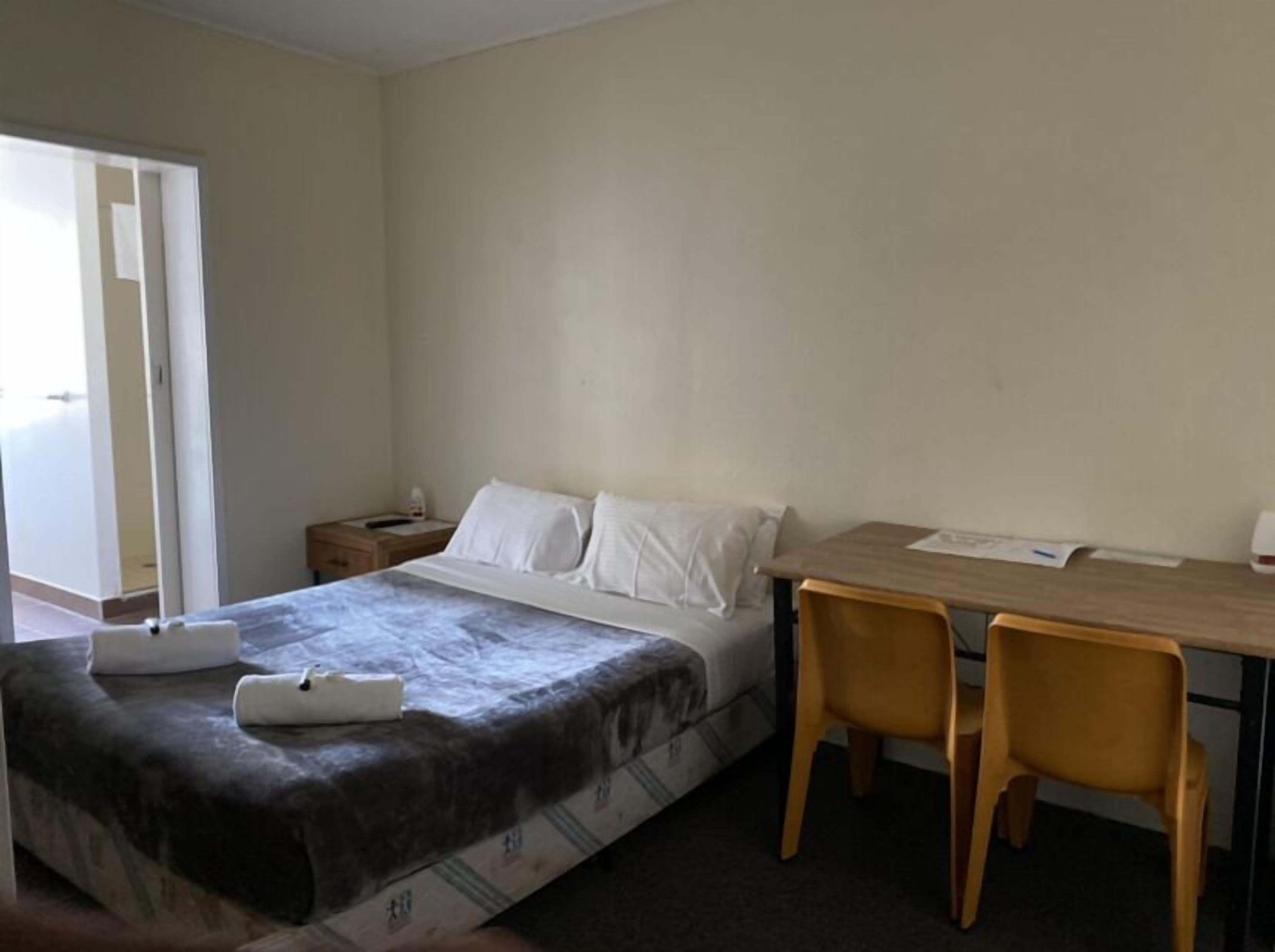 A hotel room with a bed, a desk, two chairs, a nightstand, and a door leading to a balcony.