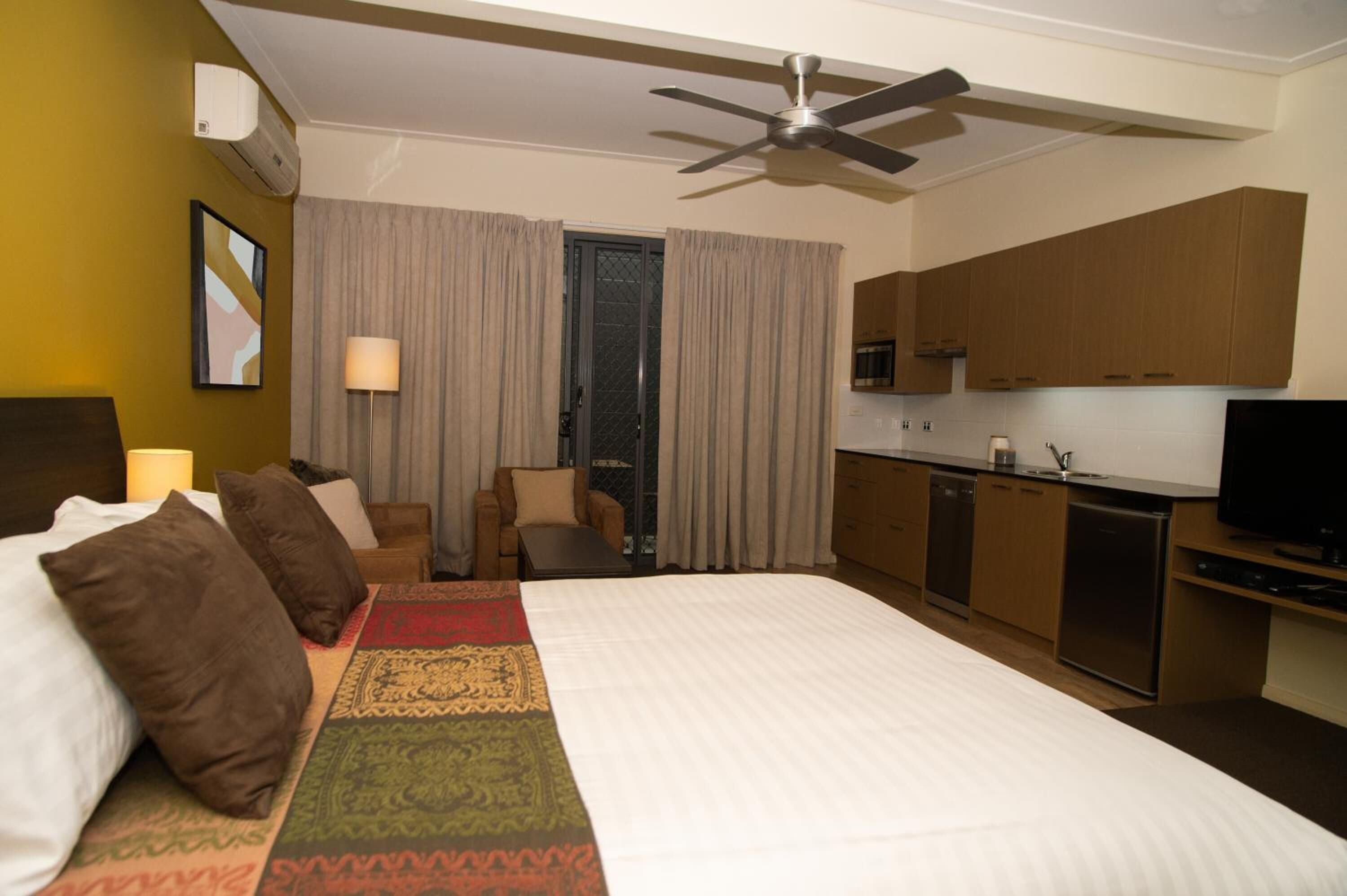 A hotel room with a bed, a desk, a chair, a television, and a kitchenette.