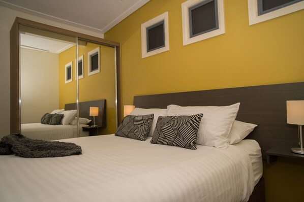A hotel room with a bed, two nightstands, a mirror, and a wall with three small windows. - Portman House (Scone)
