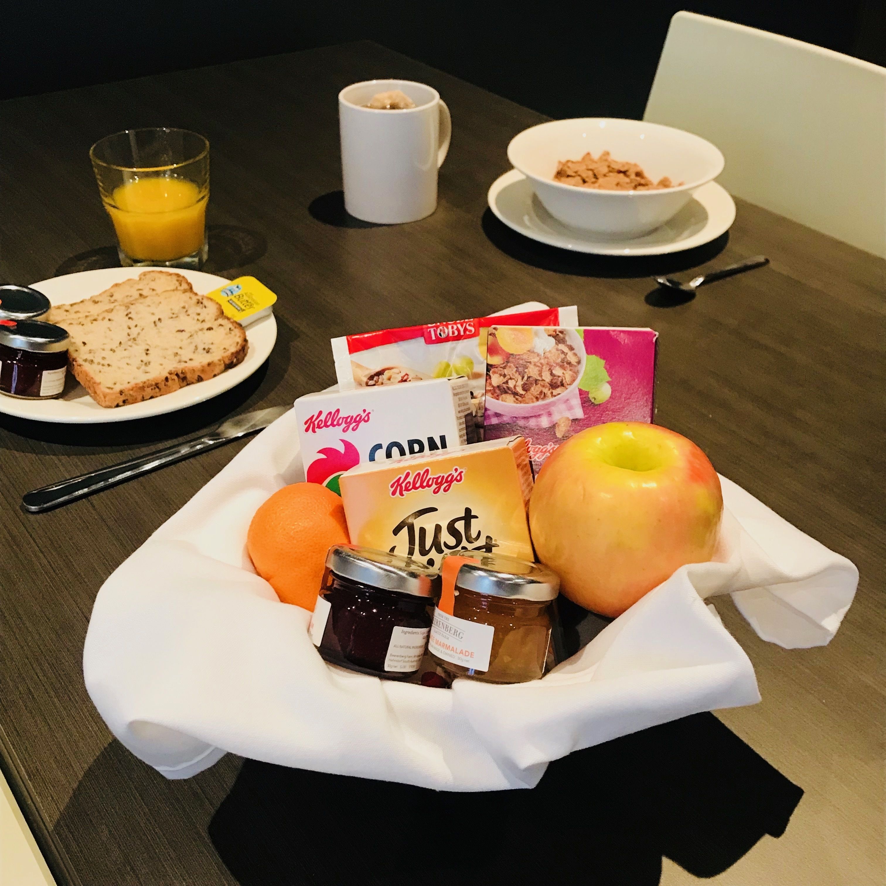A breakfast setting with toast, cereal, fruit, and condiments on a table.