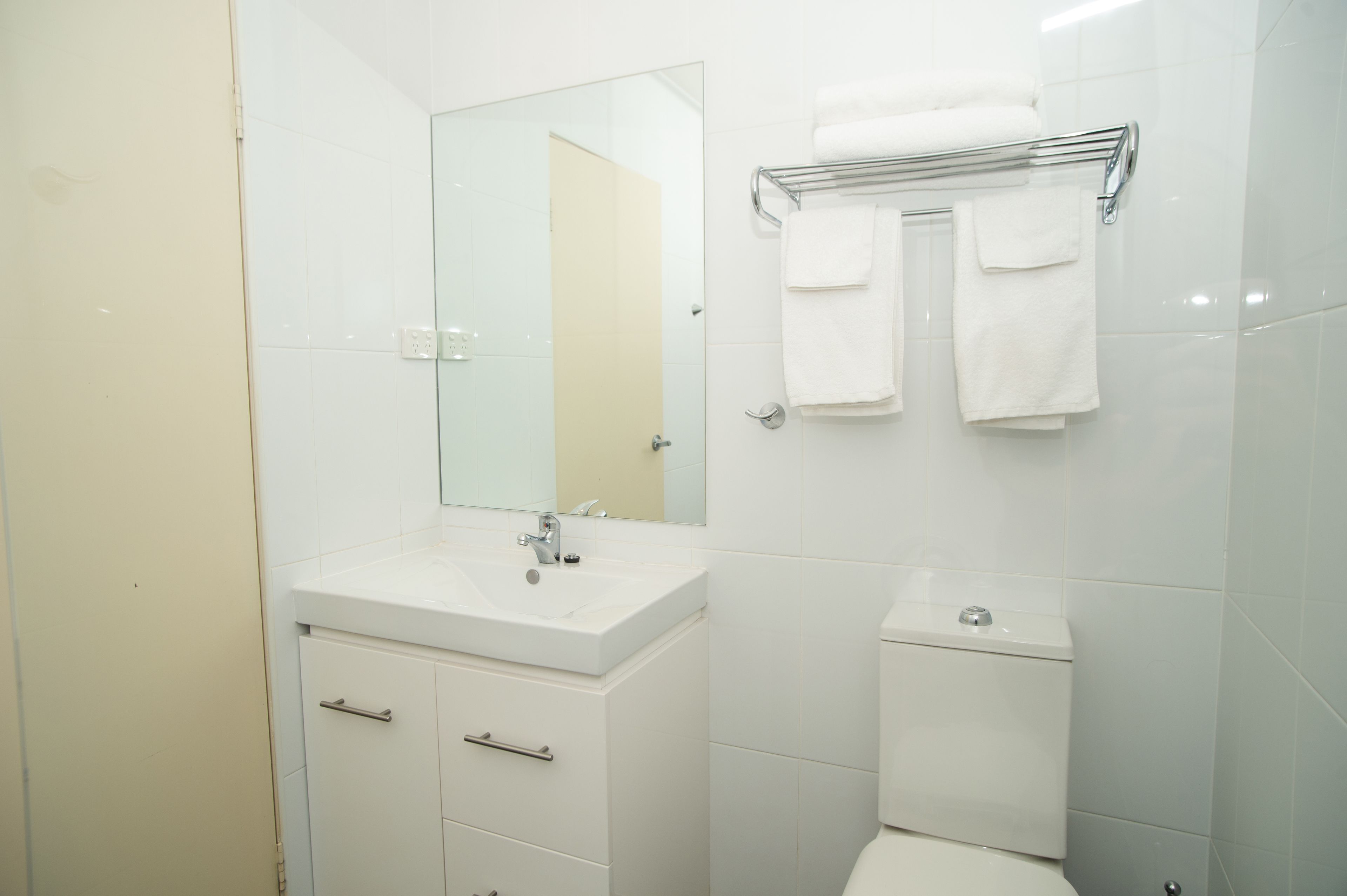 Un baño moderno con un lavamanos, espejo y retrete blancos. Dos toallas cuelgan de un tendedero.