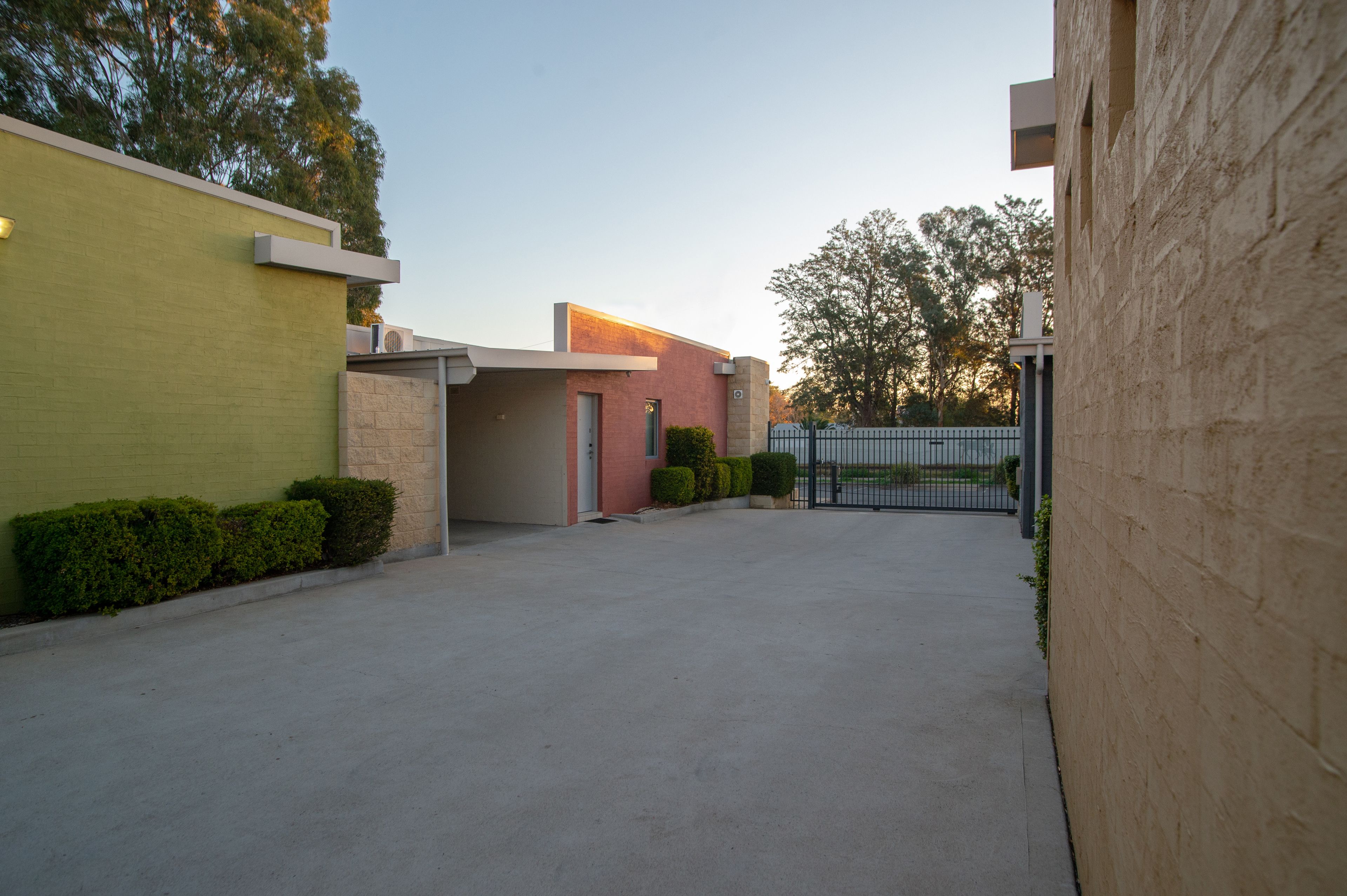 A modern building with a flat roof, a gated entrance, and a paved driveway.