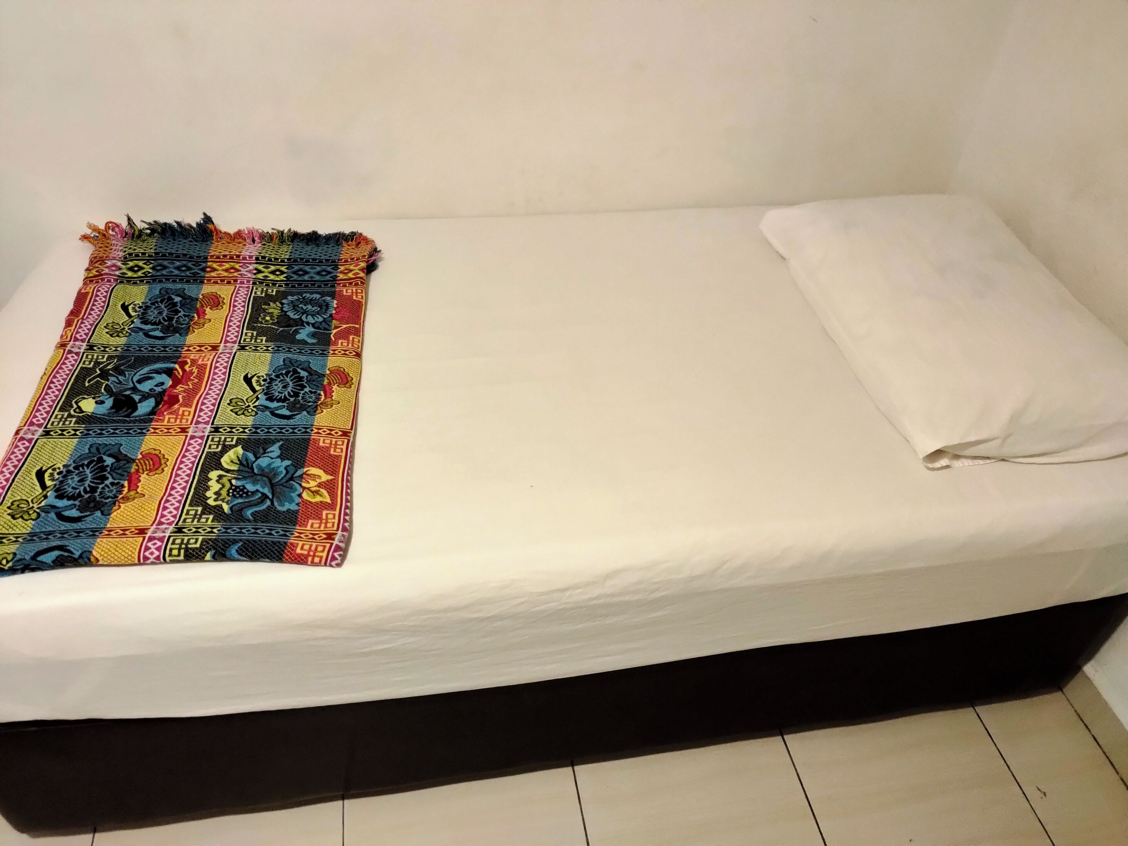 Un letto singolo con lenzuolo bianco e coperta colorata.