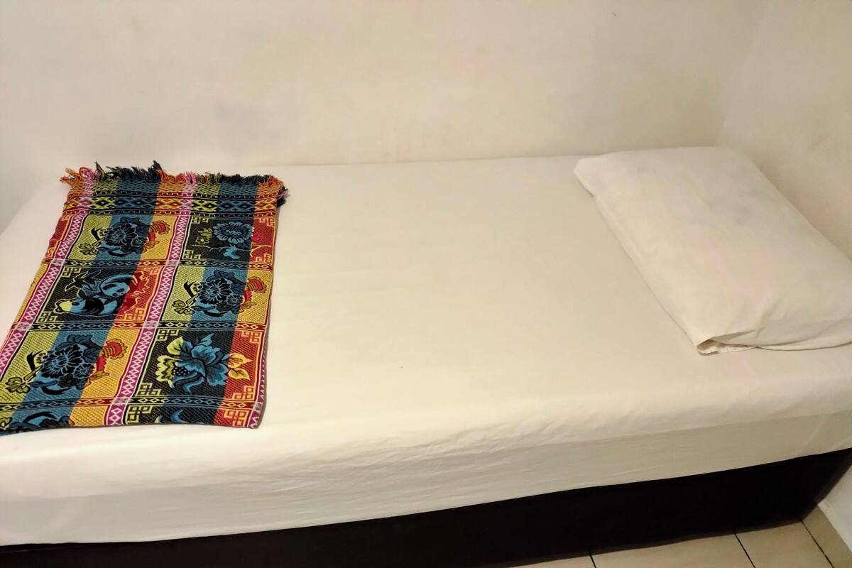 A single bed with a white sheet and a colorful blanket.
